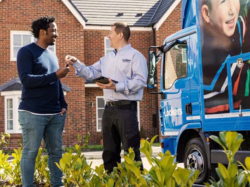 Lookers A Good Deal. Better. Care Image Block featuring a male new car delivery person handing keys over to a male customer in a residential street.