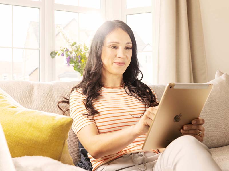 Lookers A Good Deal. Better. Choice Image Block featuring a female customer sitting on a couch while scrolling on an IPad searching Used Cars near me on Lookers.co.uk