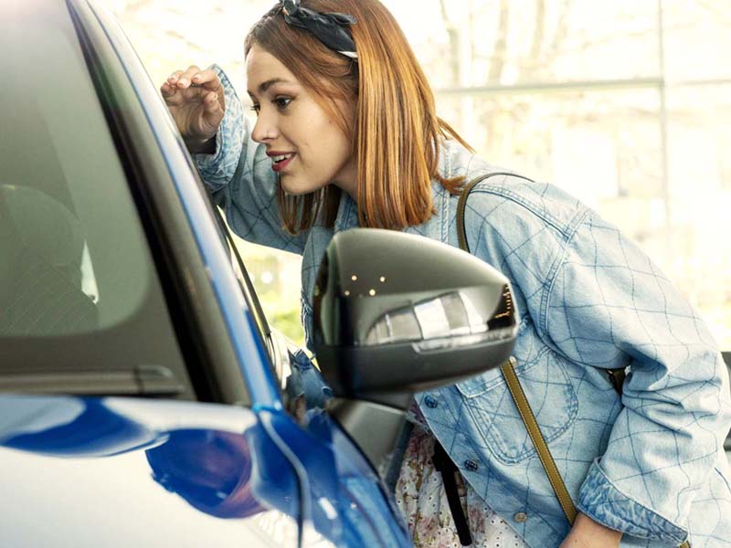 Lookers A Good Deal. Better. Transparent Pricing Image Block featuring a female customer peering through a new vehicle passenger side window when shopping for a new car in a Lookers Dealership.