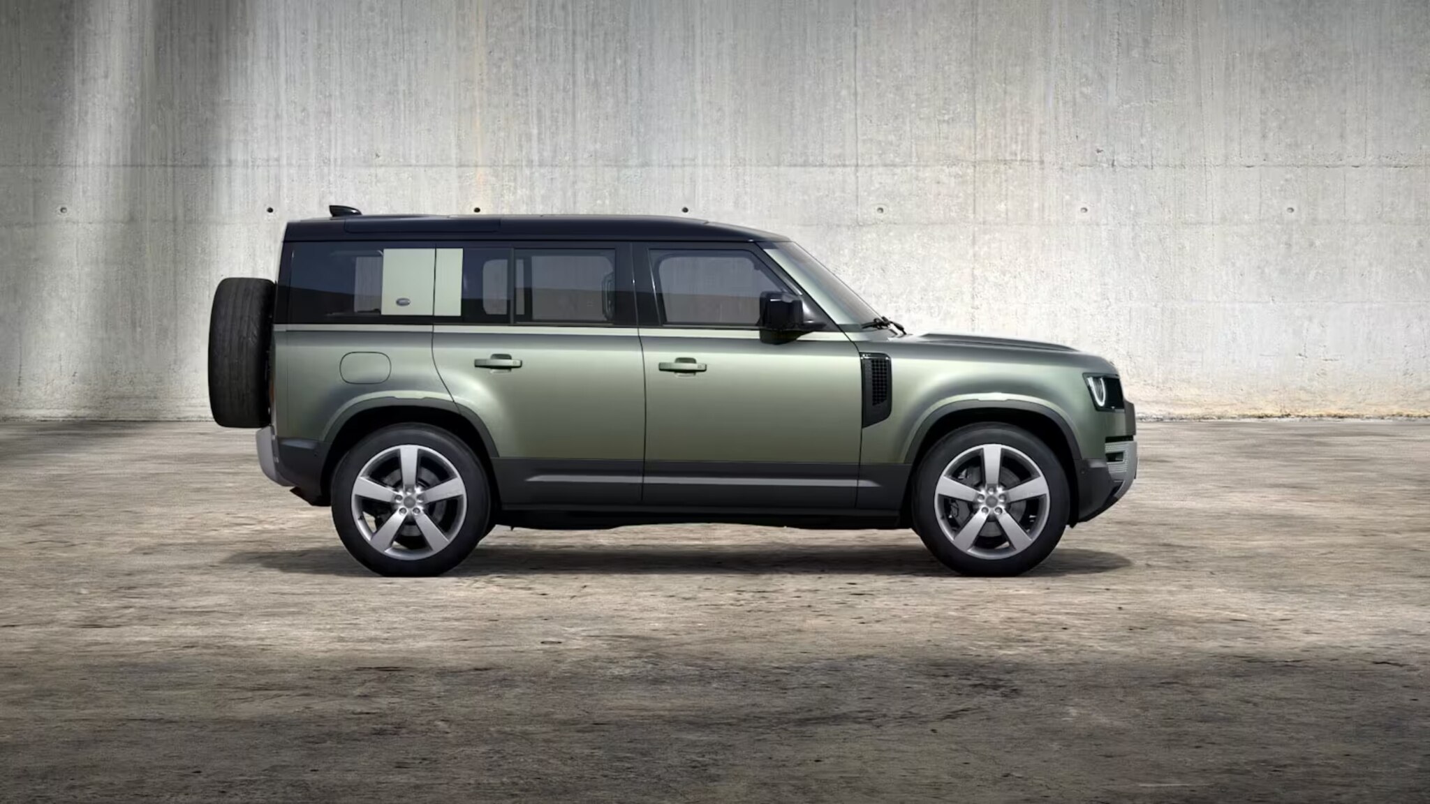 Green Defender 110 side on with grey wall in background